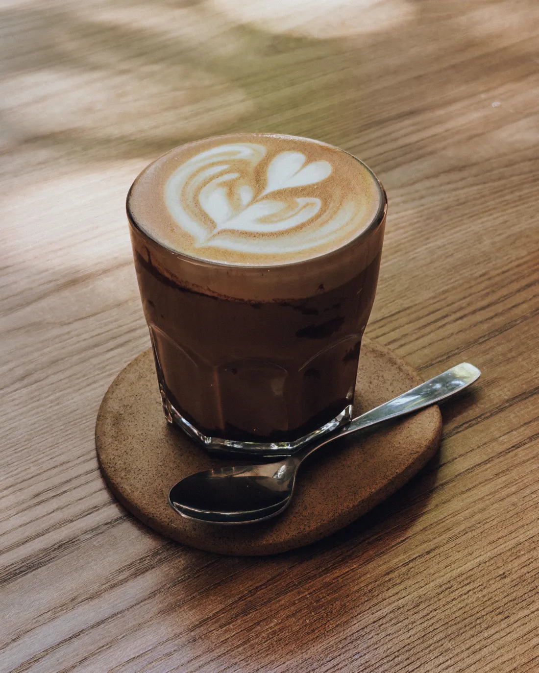 Café con leche con arte latte sobre mesa de madera (imagen ilustrativa)