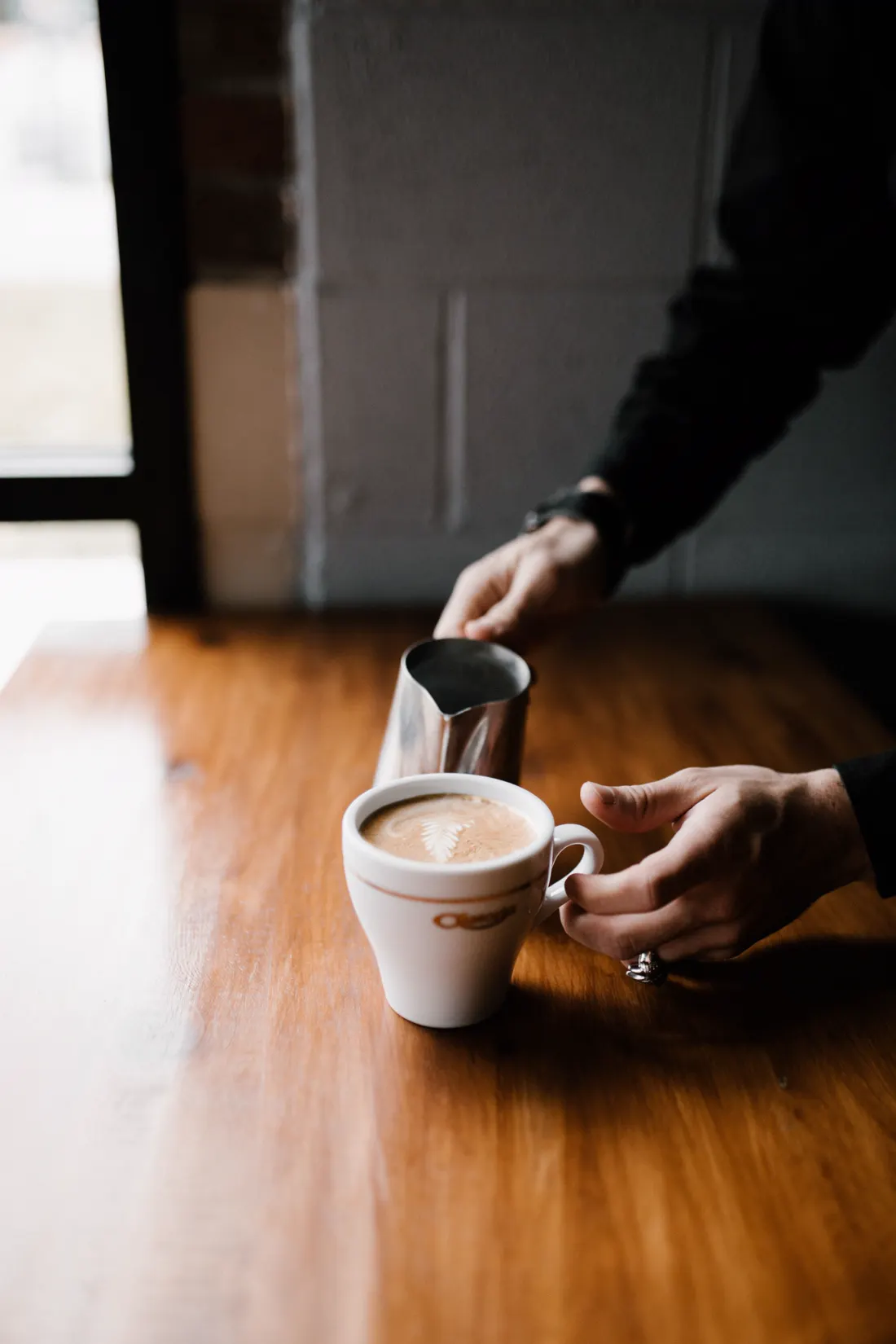 Barista sirviendo leche texturizada en una taza de café (imagen ilustrativa)
